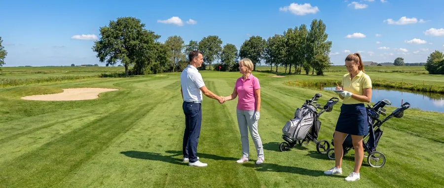 Twee golfers geven elkaar na de ronde een hand op de fairway, een derde speelster noteert de score op de scorekaart