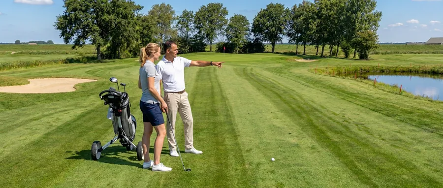 Een golfster pakt een ijzer uit haar tas terwijl de professional naar de green wijst